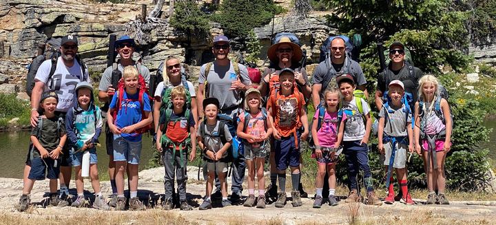Dad Camp 2020 group photo: dads and kids with backpacks lined up on the rocky shore by the lake, Long Lake trip