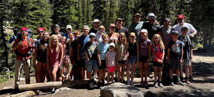 Dad Camp 2025 group photo: dads and kids gathered together on a forest trail among tall pines at Island Lake